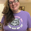 A smiling woman with glasses wearing a purple graphic t-shirt that reads 'JUDGE ME YOU'RE NOT MY CAT' with a black and white cat illustration.